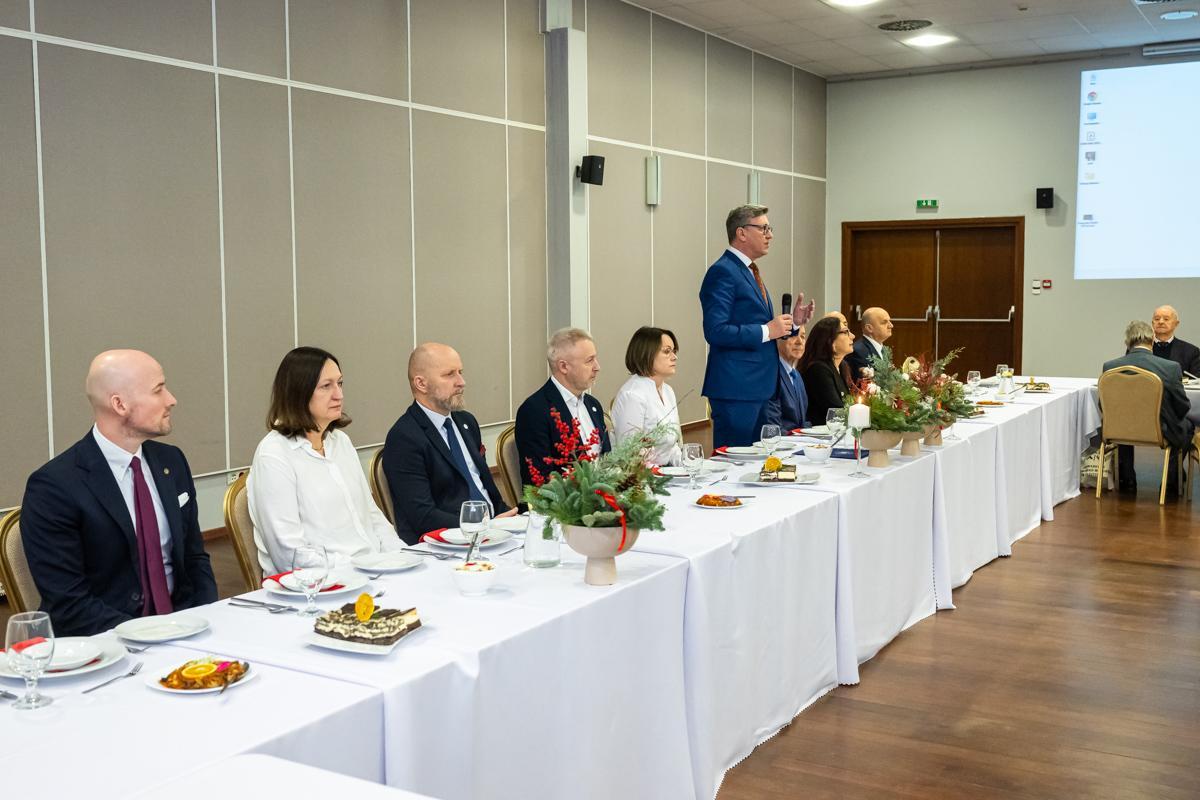 Władze uczelni siedzą za stołem na spotkaniu opłatkowym z profesorami 