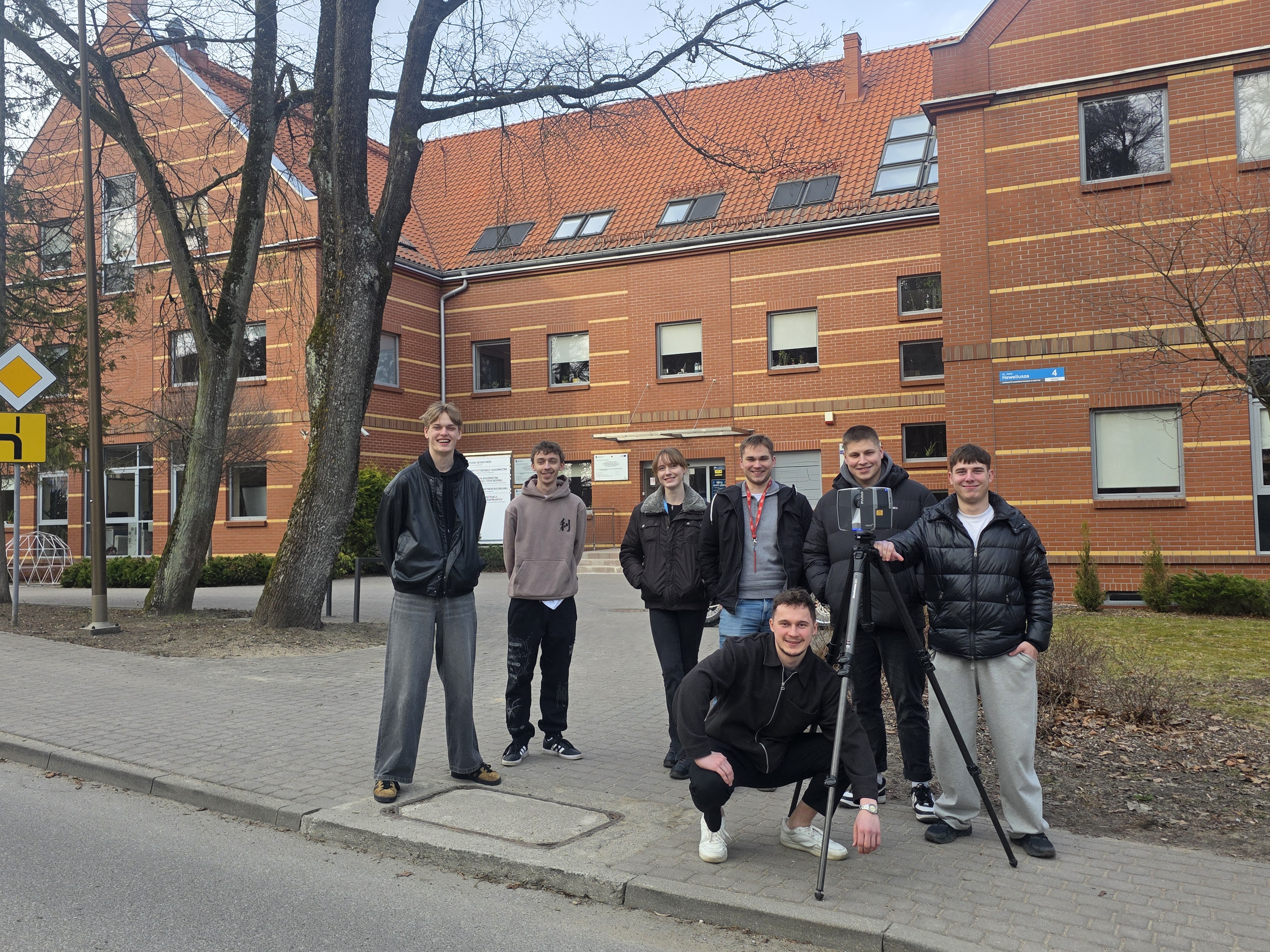 uczestnicy BIP podczas pracy ze skanerem laserowym pozują do zdjęcia przed budynkiem Wydziału Geoinżynierii