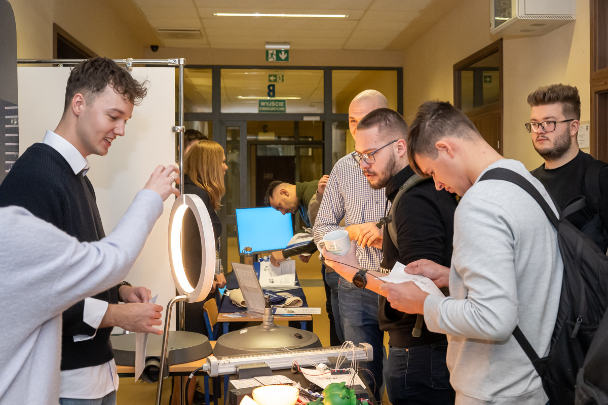 studenci stoją naprzeciwko stoiska i zbierają informacje o firmie