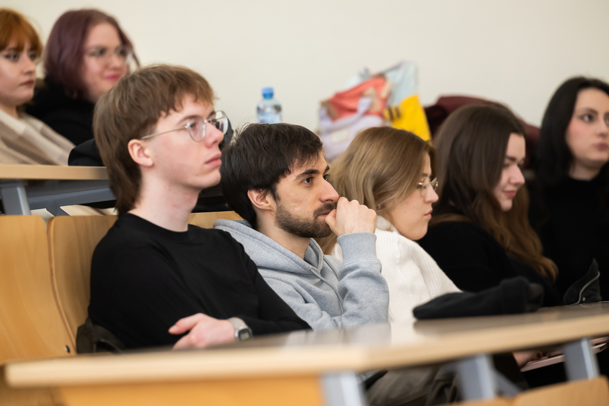 studenci siedzą w ławkach i słuchają wykładu