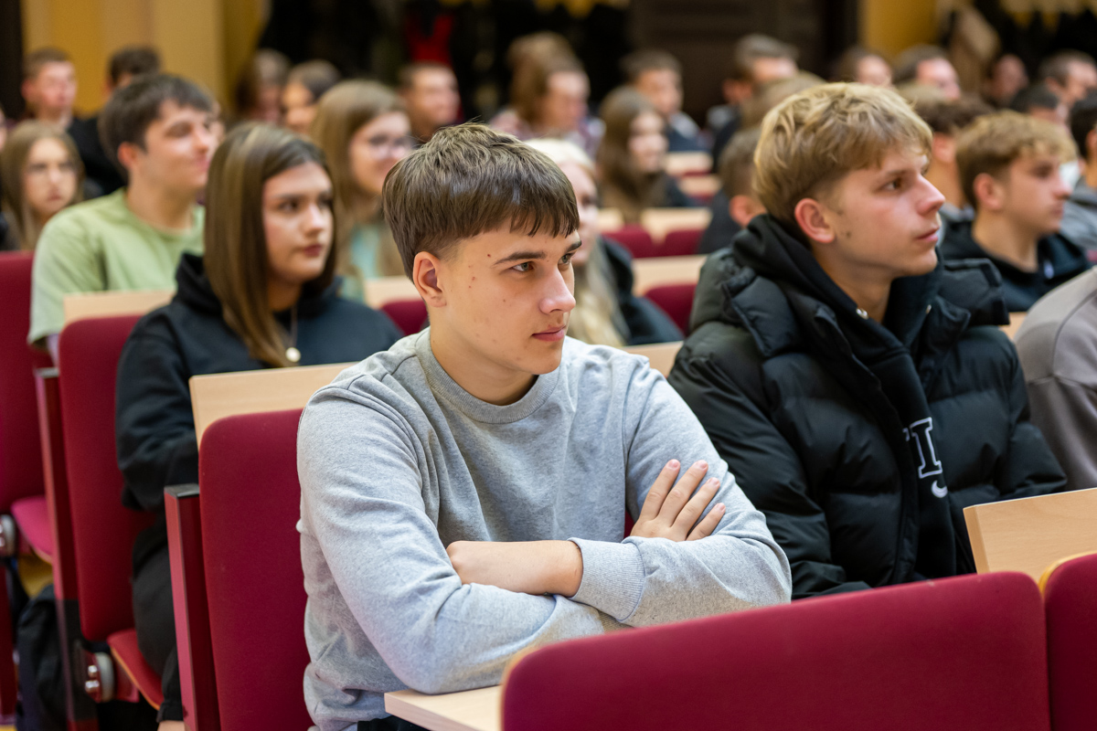 studenci siedzą w ławkach i słuchają wykładu