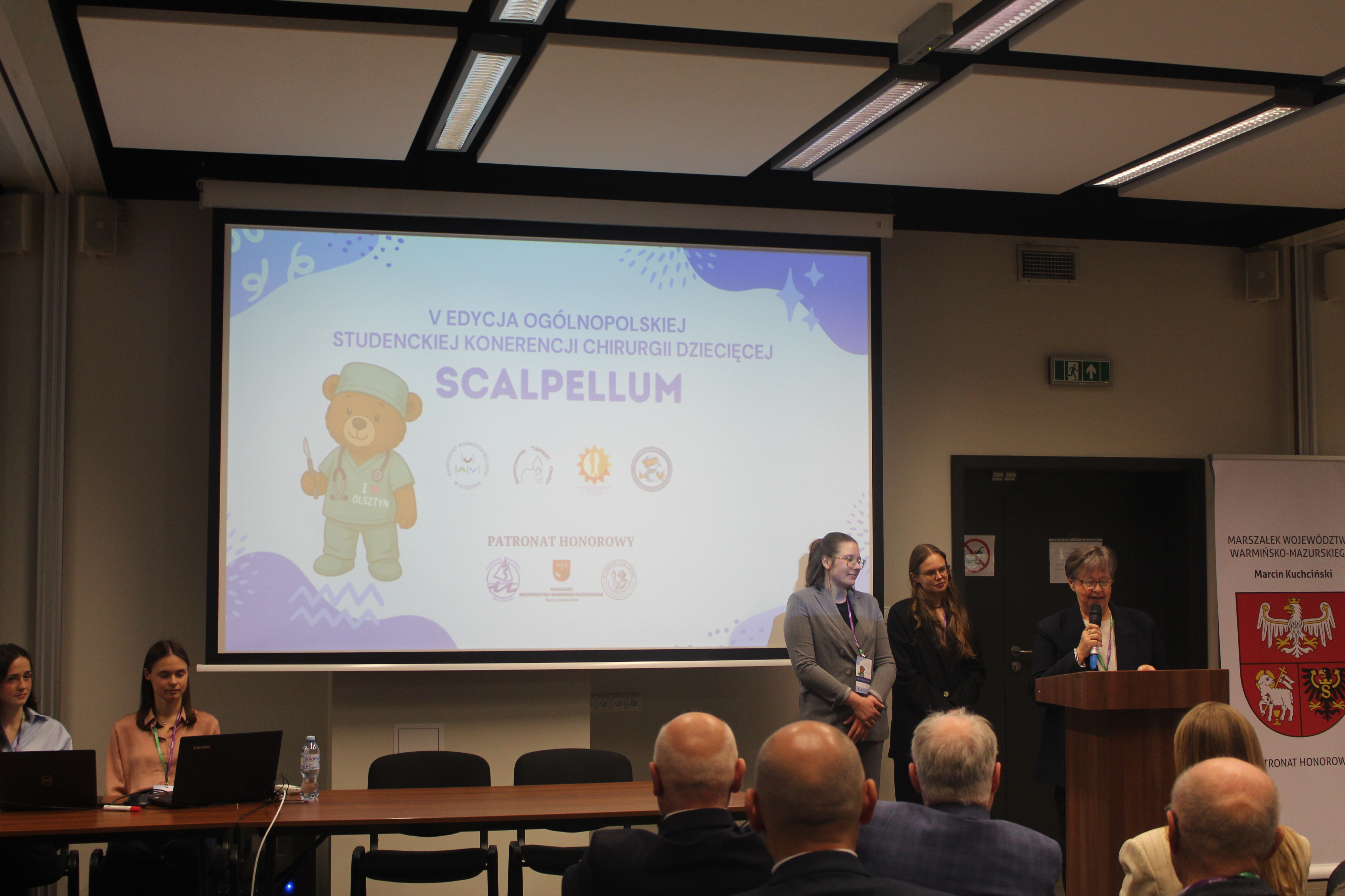 Rozpoczęcie konferencji, prelegentka przemawia, w tle ekran z logo wydarzenia