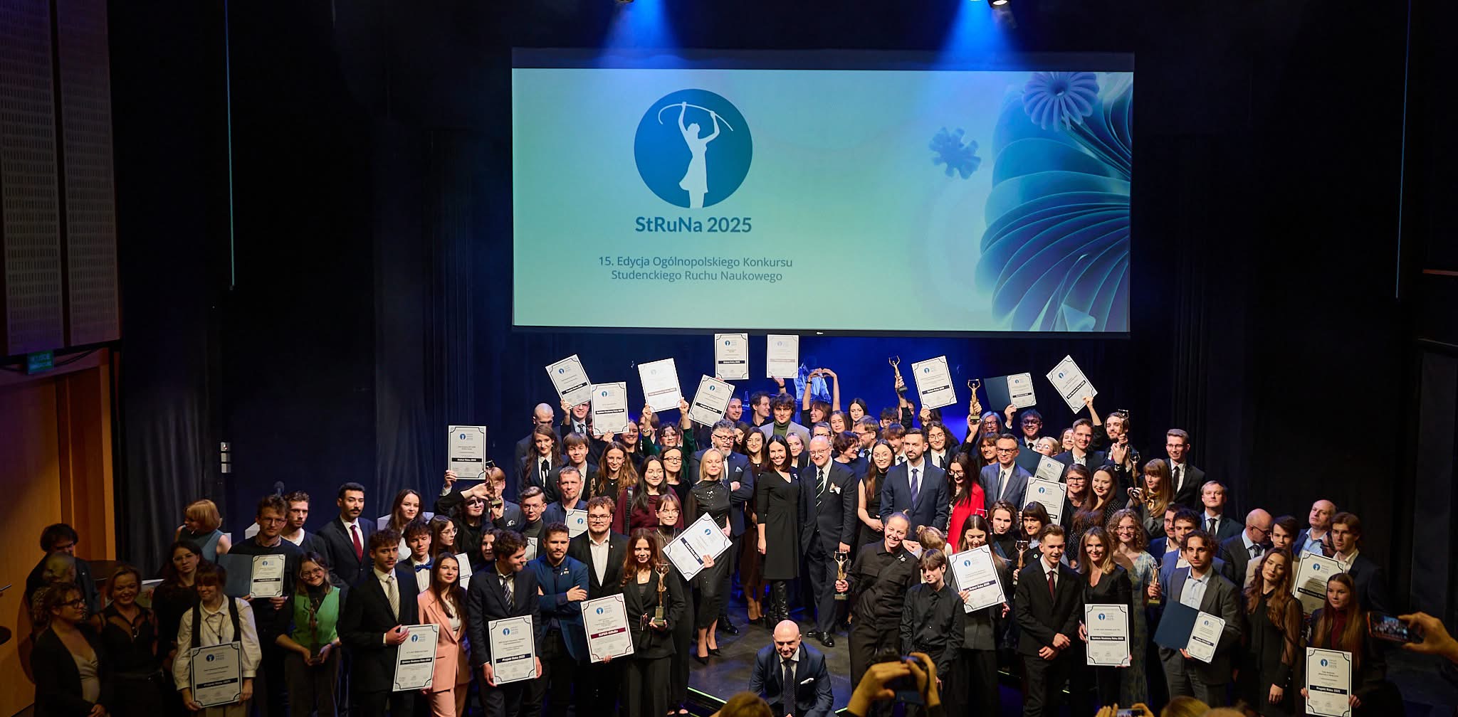 Duża grupa osób nagrodzona w 15. Ogólnopolskim Konkursie Studenckiego Ruchu Naukowego StRuNa pozuje do zdjęcia z dyplomami