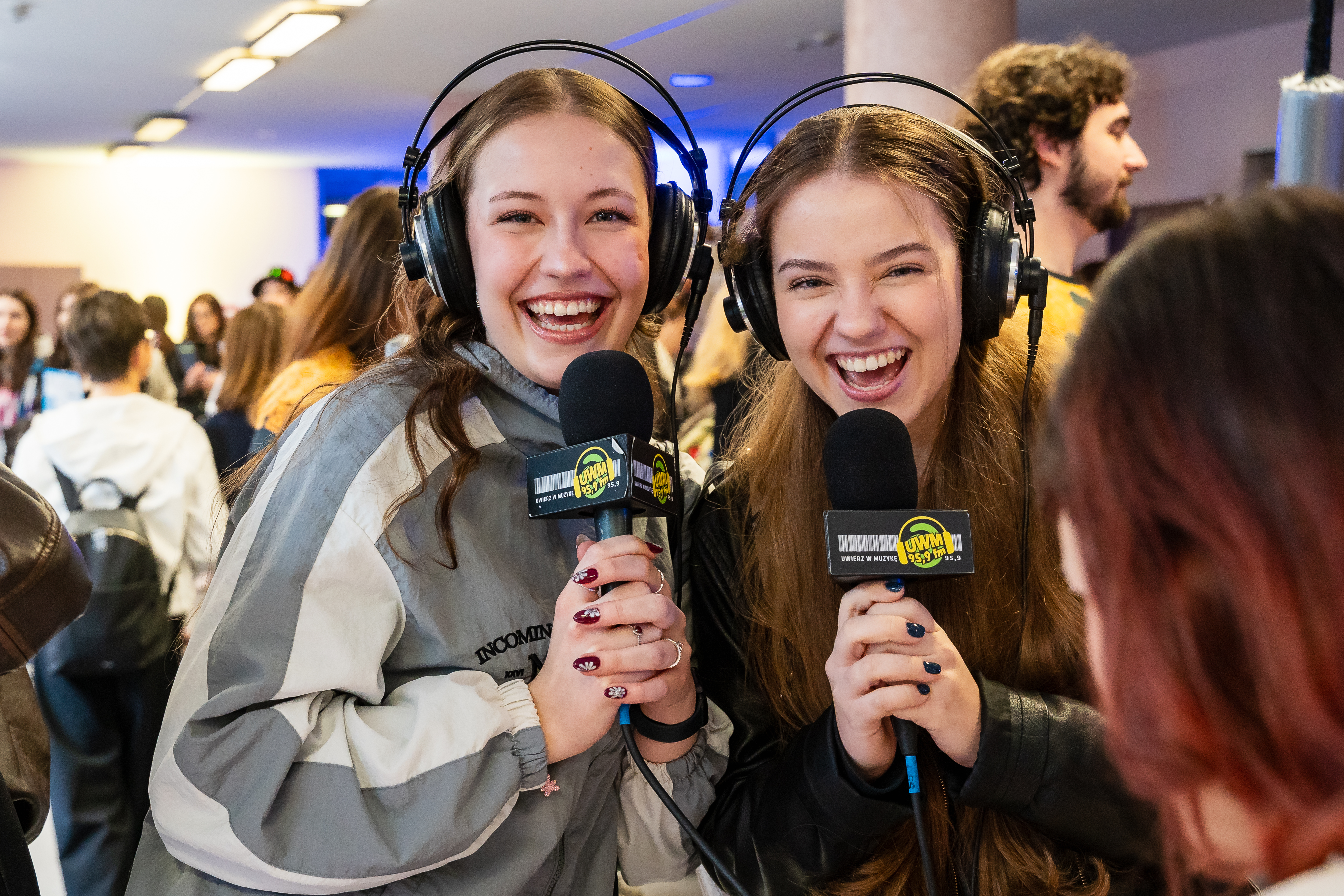 Dwie uśmiechnięte dziewczyny pozują do zdjęcia, trzymając w dłoniach mikrofony Radia UWM FM