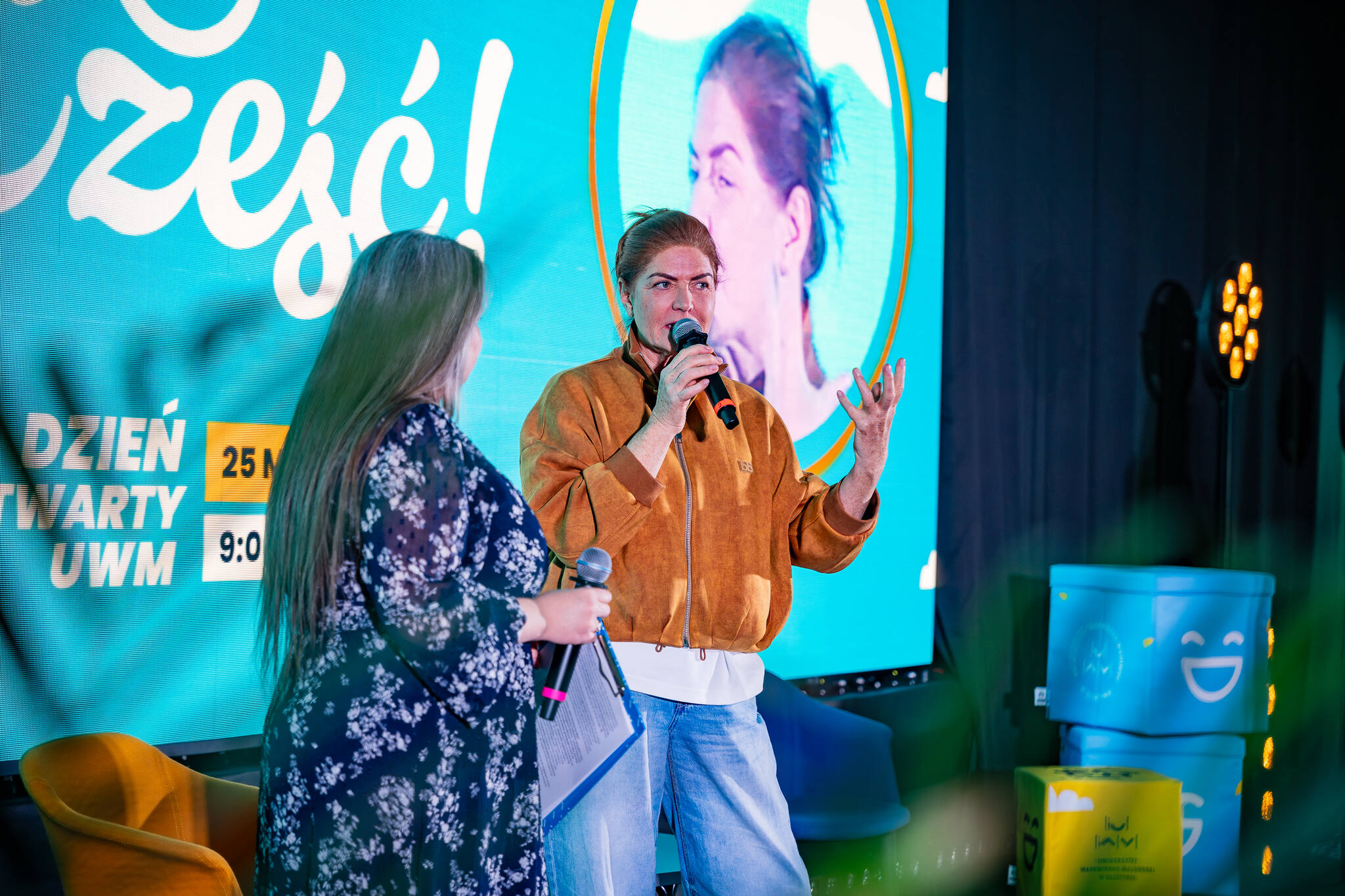 Katarzyna Dowbor na scenie podczas Dnia Otwartego UWM. Po lewej stronie stoi też prowadząca spotkanie