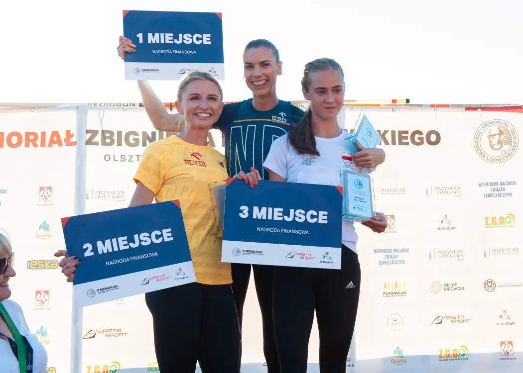 Trzy dziewczyny stoją na podium i trzymają kartki z numerami 3 pierwszych miejsc
