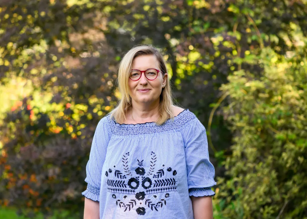 Agnieszka Jaszczak stoi wśród drzew w niebieskiej bluzce 