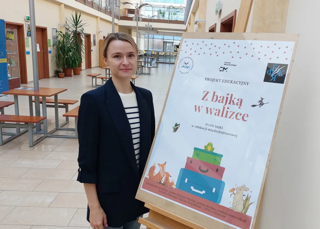 Joanna Olechno-Wasiluk stoi przy plakacie o projekcie "Z bajką w walizce"