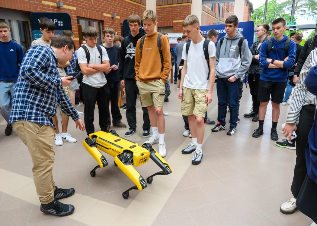 studenci stoją i patrzą na robota psa