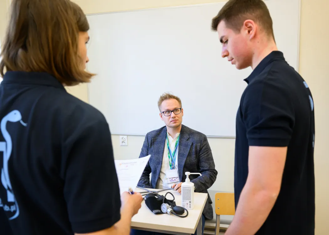 studenci stoją przed  członkiem komisji konkursowej