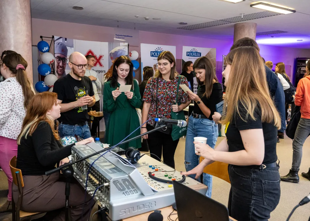 pięć osób, mężczyźni i kobiety stoją przed konsolą do nagrywania audycji radiowych