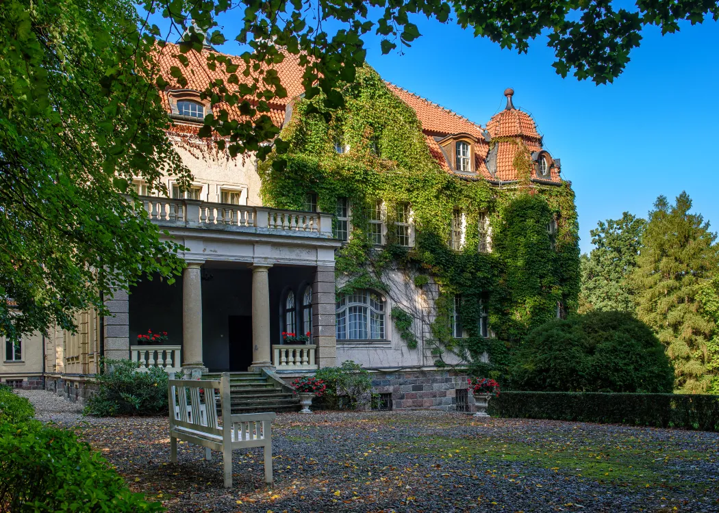 zdjecie przedstawiajace palac w lezanach od zewnatrz z biala laweczka przed budynkiem