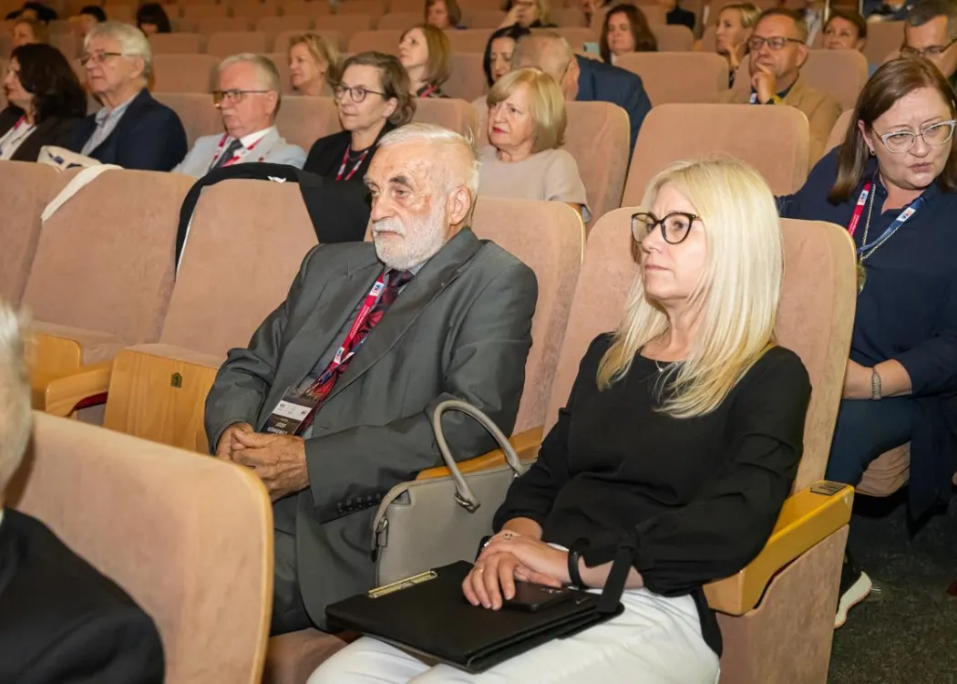 Zjazd pedagogiczny: goście siedzą w sali, na pierwszym planie starszy mężczyzna z kobietą