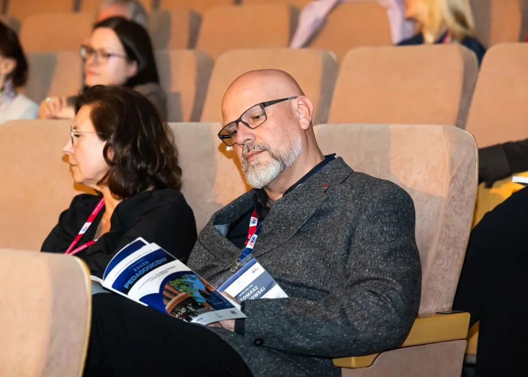 Zjazd pedagogiczny: goście siedzą w sali, na pierwszym planie mężczyzna w okularach