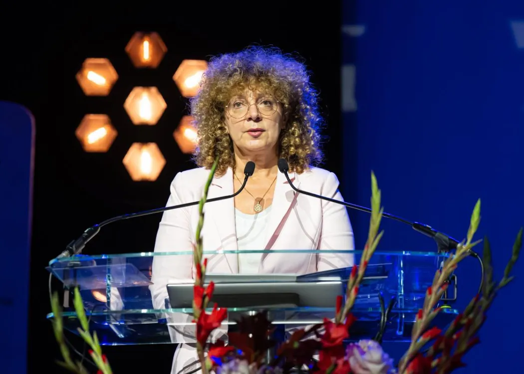 Zjazd pedagogiczny: kobieta w białym stroju przemawia do mikrofonu