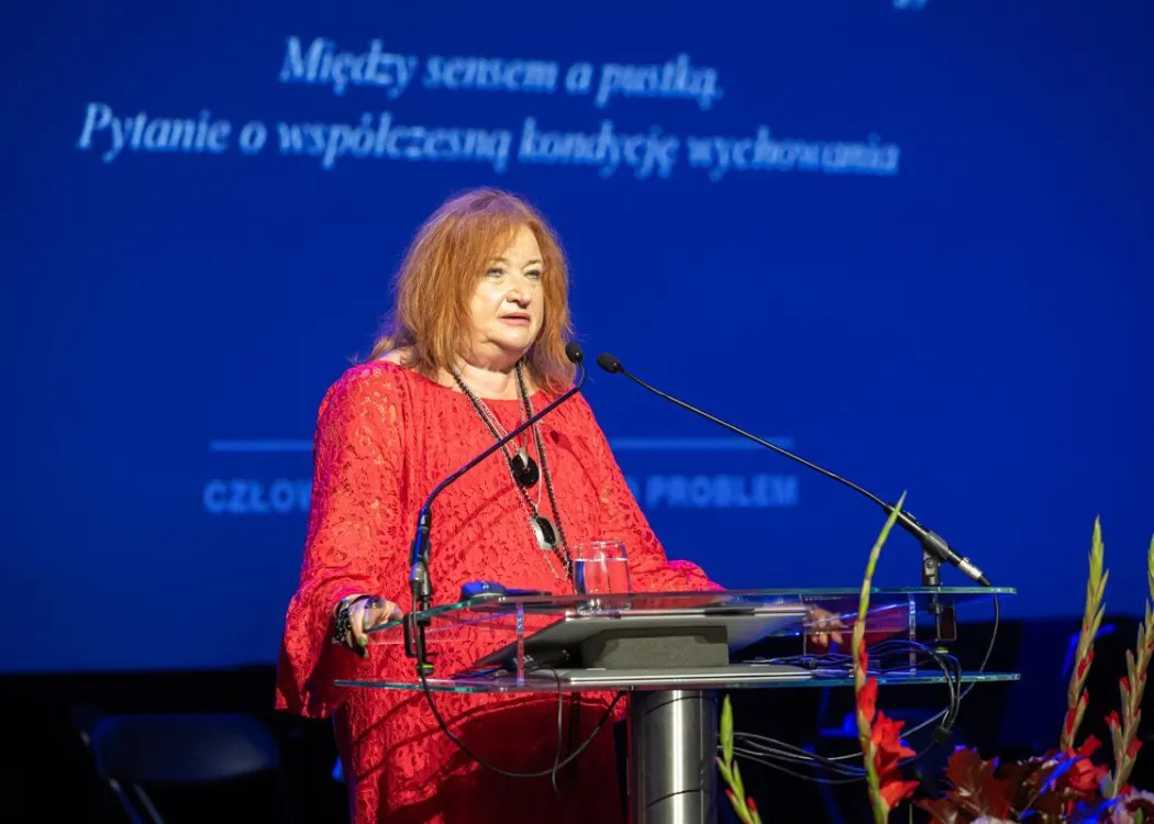 Zjazd pedagogiczny: kobieta w czerwonej sukni przemawia do mikrofonu