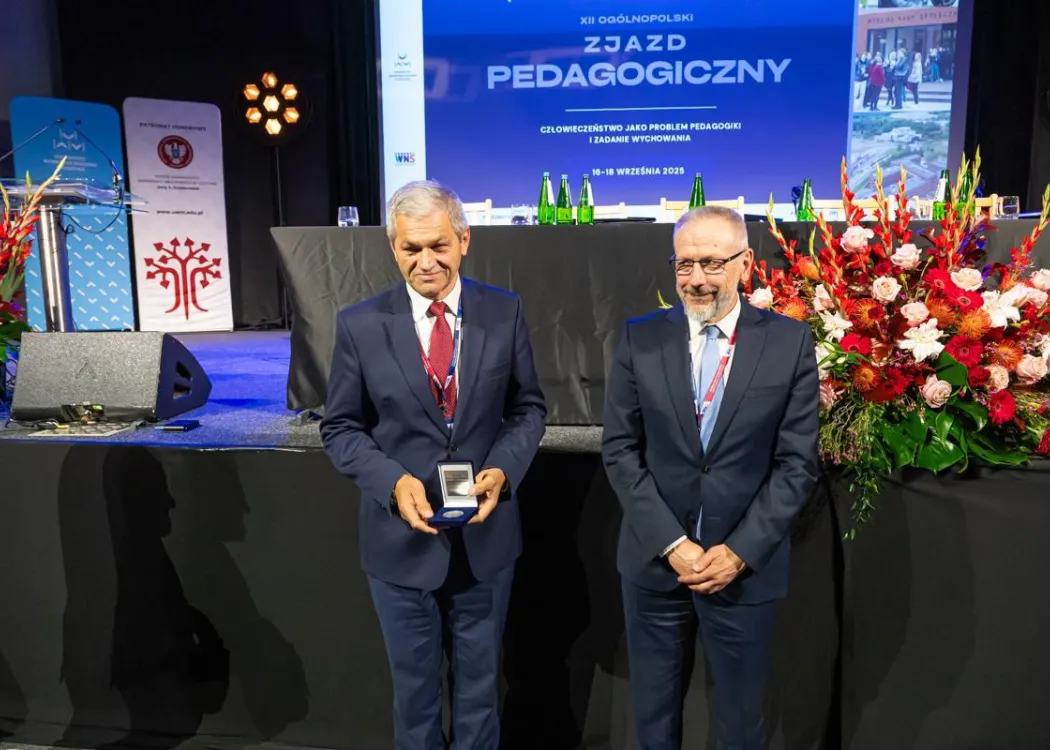 Zjazd pedagogiczny: dwóch mężczyzn w garniturach stoi, jeden z medalem w futerale