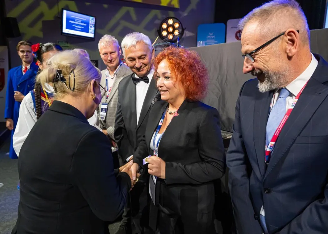 Zjazd pedagogiczny: kilka osób stoi przed sceną, uściski dłoni