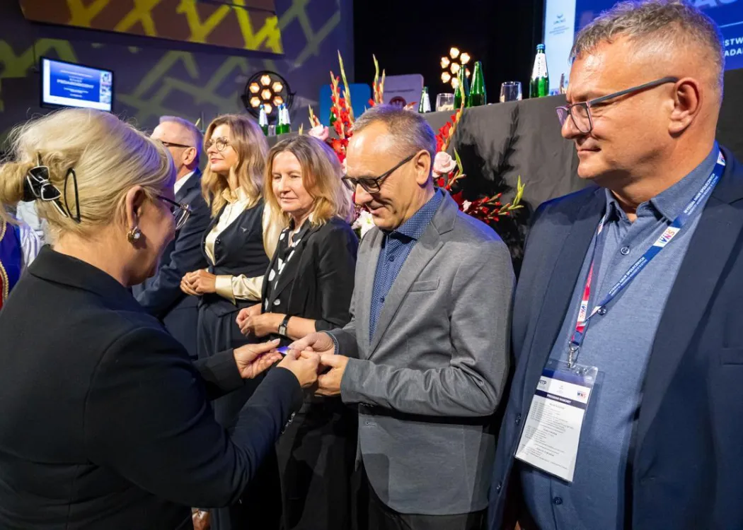 Zjazd pedagogiczny: kilka osób stoi przed sceną, uściski dłoni