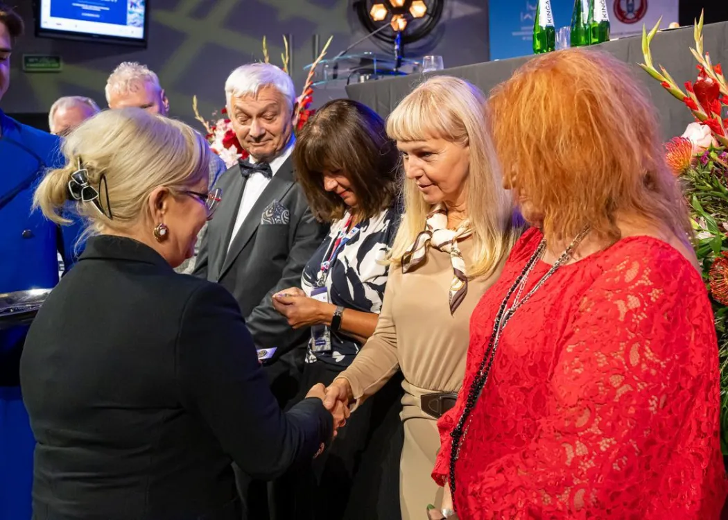 Zjazd pedagogiczny: uścisk dłoni kobiecie, w tle stoi kilka osób