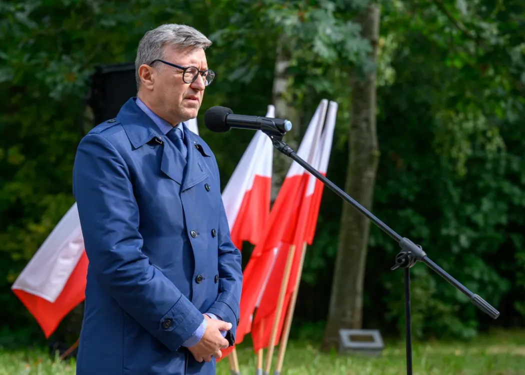 Rektor przemawia do mikrofonu na tle flag Polski