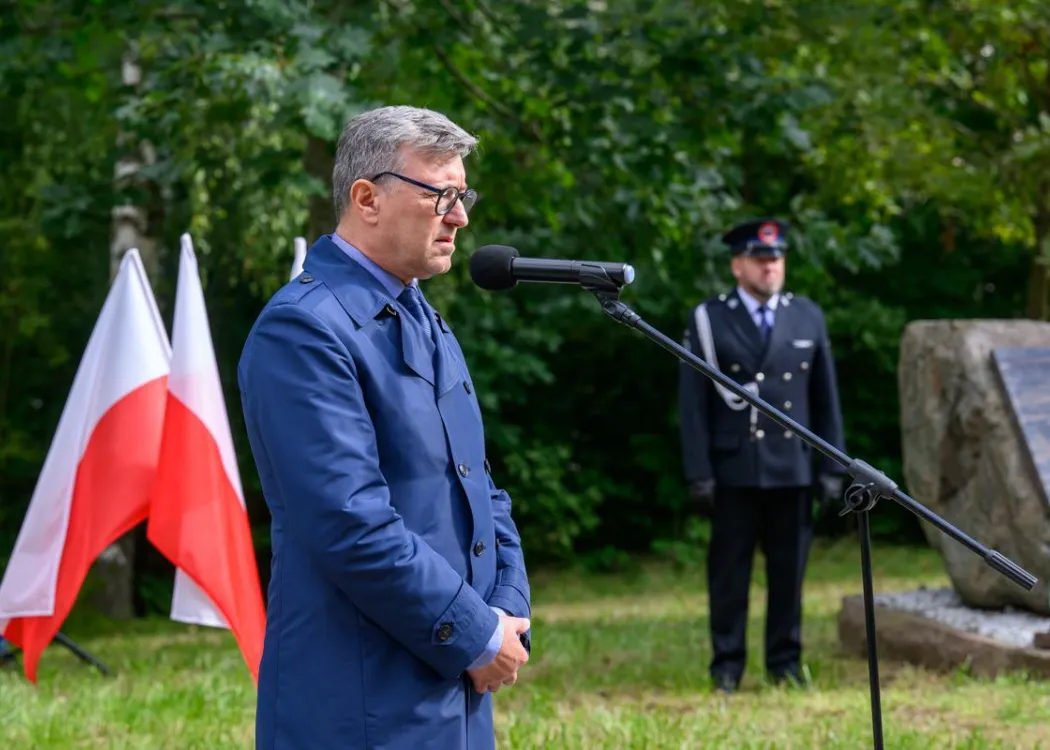 rektor UWM przemawia do mikrofonu, obok flaga Polski i głaz