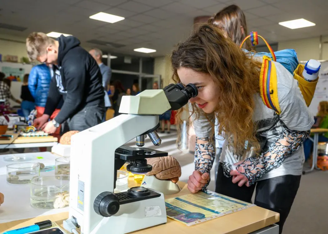 Student EXPO 2025: uczestniczka patrzy przez mikroskop na jednym ze stoisk 