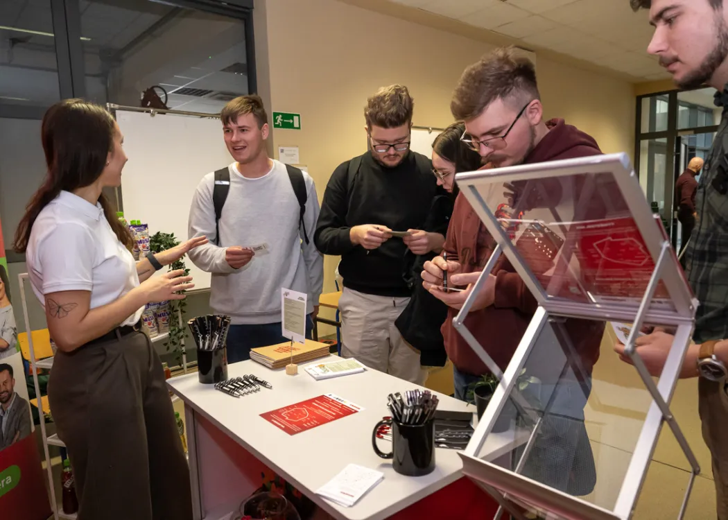 studenci stoją naprzeciwko stoiska i zbierają informacje o firmie
