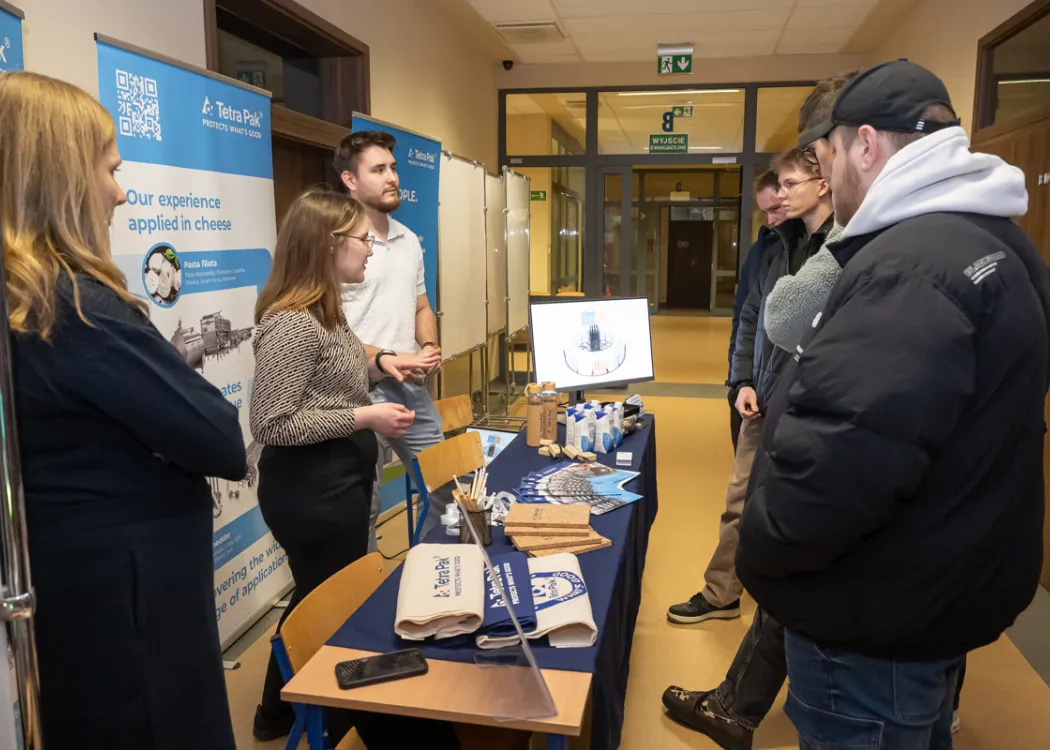 studenci stoją naprzeciwko stoiska i zbierają informacje o firmie