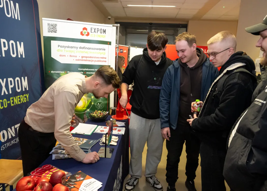 studenci stoją naprzeciwko stoiska i zbierają informacje o firmie
