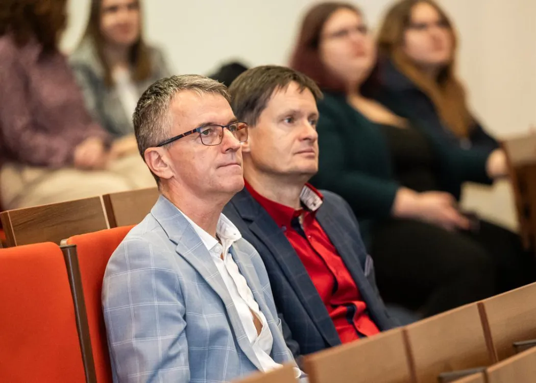 GIS Day 2025: prodziekan Wydziału Geoinżynierii wraz z innym mężczyzną słuchają prelekcji 