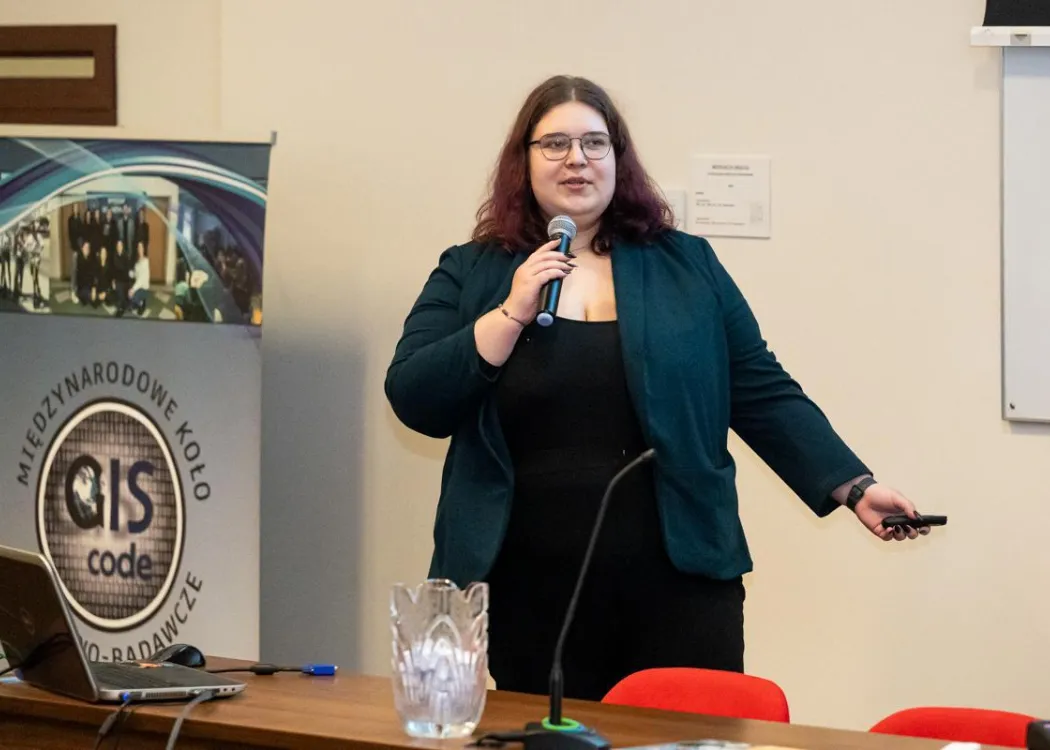 GIS Day 2025: studentka z koła naukowego stoi z mikrofonem, wygłaszając referat 