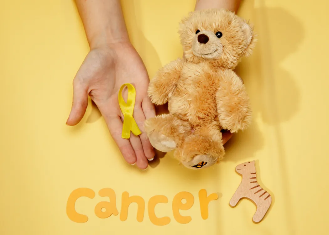 Zdjęcie ilustracyjne z napisem "cancer" przedstawia misia i dłoń, na której leży złota wstążką