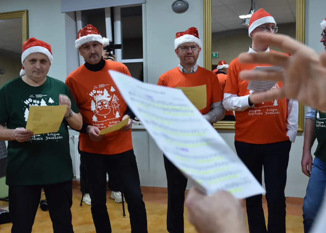 Nagranie pastorałki 2025: kartka papieru z nutami, a na drugim planie mężczyźni nagrywający pastorałkę