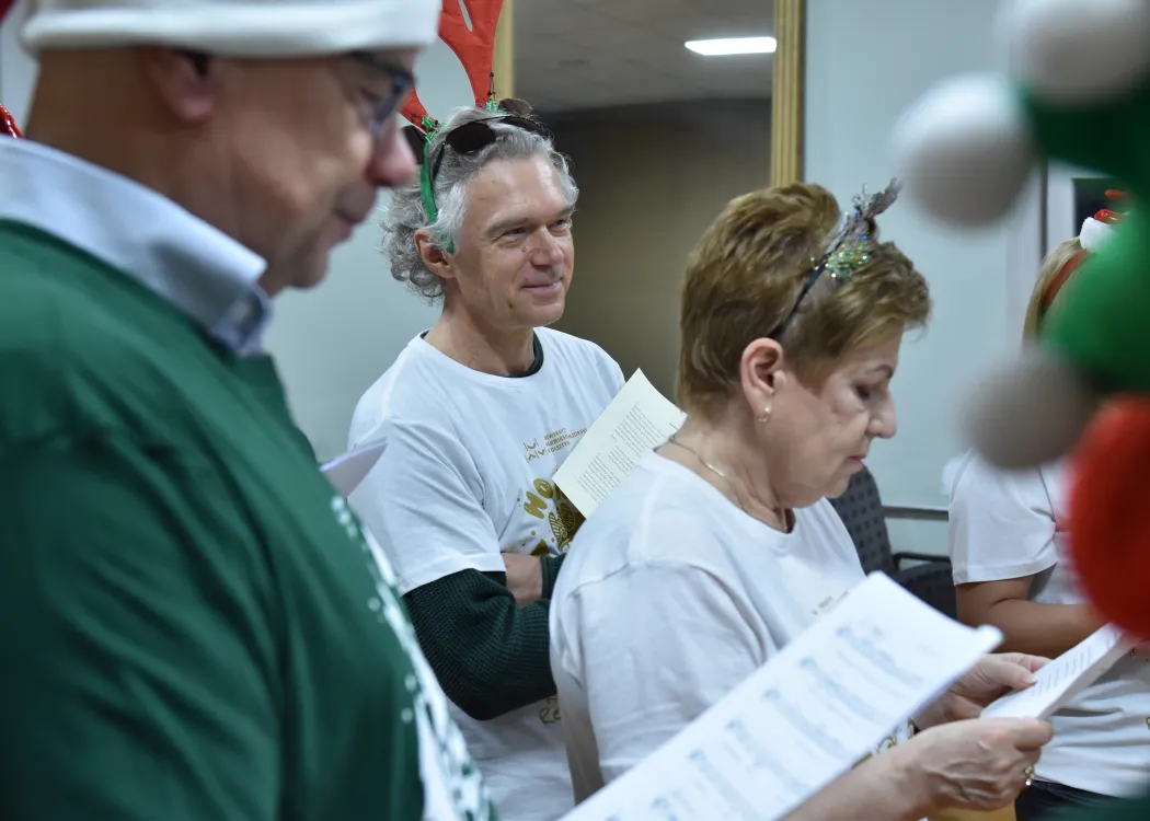 Nagranie pastorałki 2025: kartka papieru z nutami, a w tle uczestnicy nagrania pastorałki 