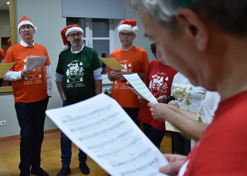 Nagranie pastorałki 2025: kartka papieru z nutami, a w tle uczestnicy nagrania pastorałki 