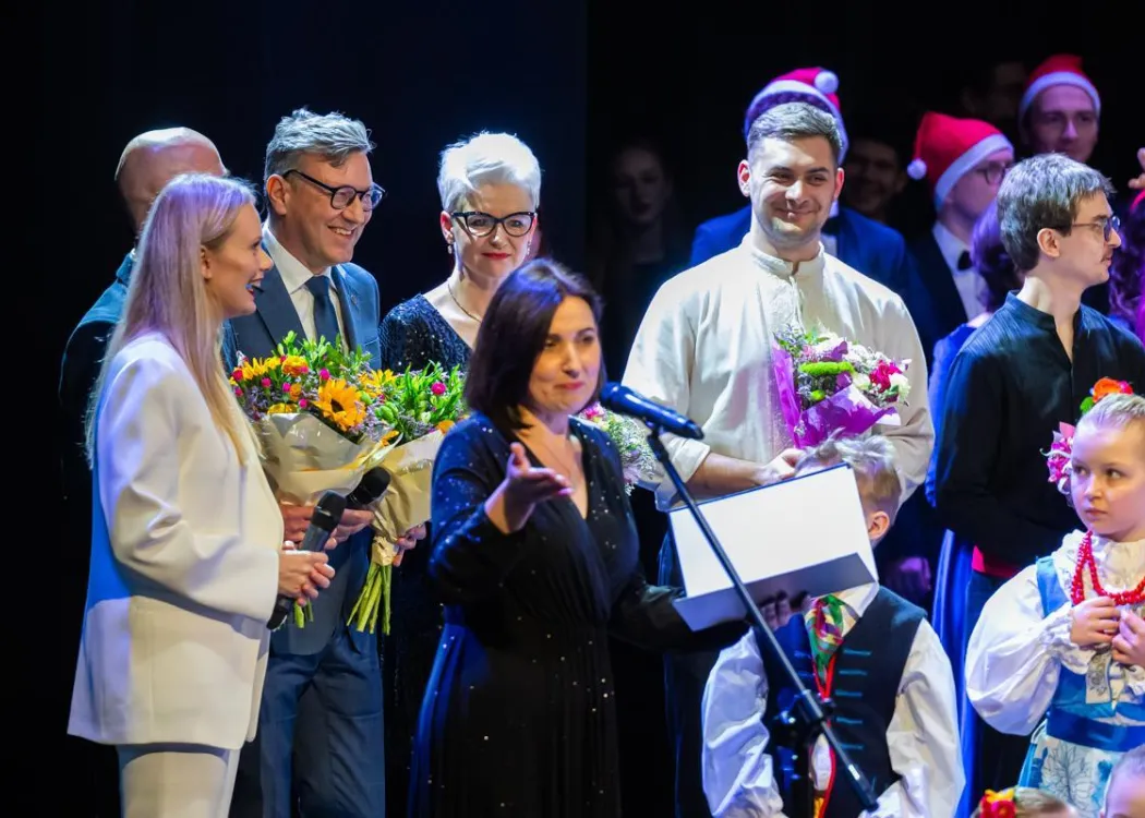 Koncert Kultura pod choinkę 2025: władze rektorskie i wykonawcy patrzą na przemawiającą do publiczności prowadzącą koncert