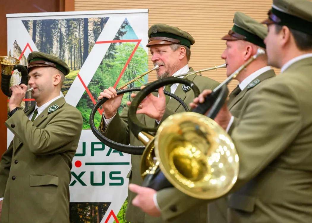 Zdjęcie przedstawia leśników ubranych w mundurach galowych i grających na instrumentach