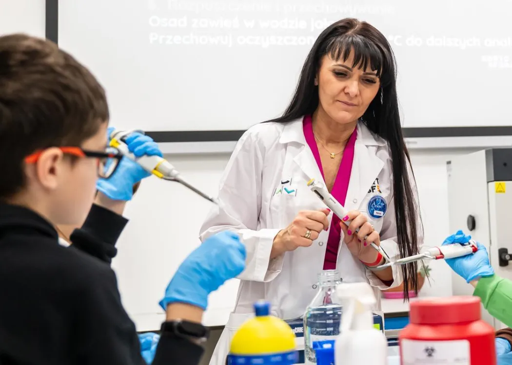 Noc Biologów 2026: prowadząca zajęcia, pojemniki z płynami i uczestnicy