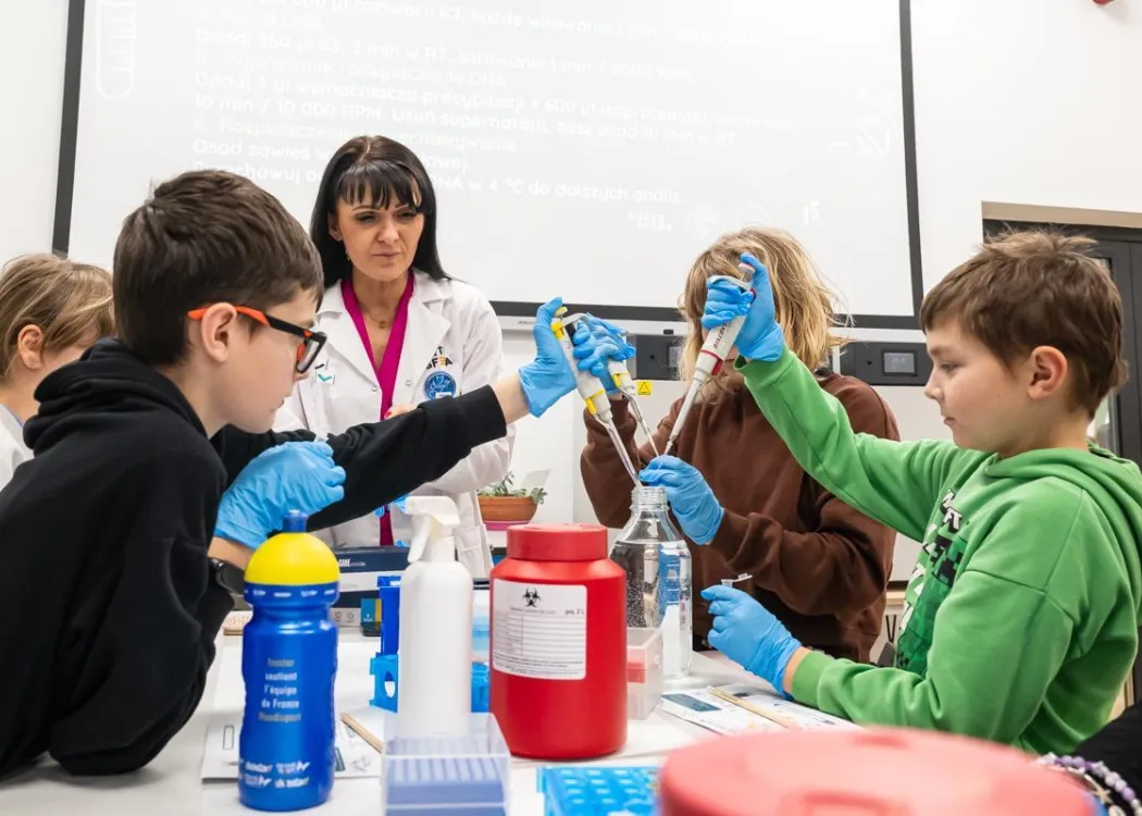 Noc Biologów 2026: uczestnicy pobierają przyrządami płyn z pojemników 