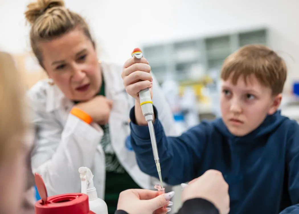 Noc Biologów 2026: chłopiec ze sprzętem laboratoryjnym i prowadzącą zajęcia