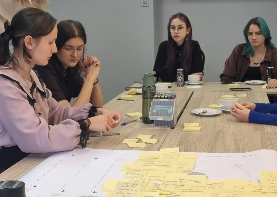 studentki siedzą przy stole, na którym są rozłożone różne kartki z pomysłami