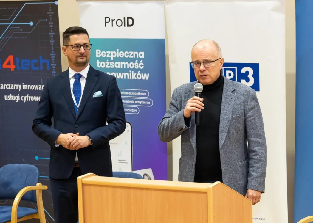 Dziekan Wydziału Matematyki i Informatyki trzyma mikrofon i przemawia, a Łukasz Strzelecki z Cyberdot patrzy w jego stronę