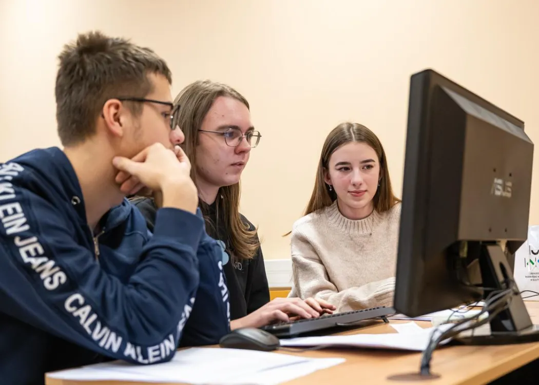 Młodzież siedzi przy komputerze podczas zespołowych zawodów programowania