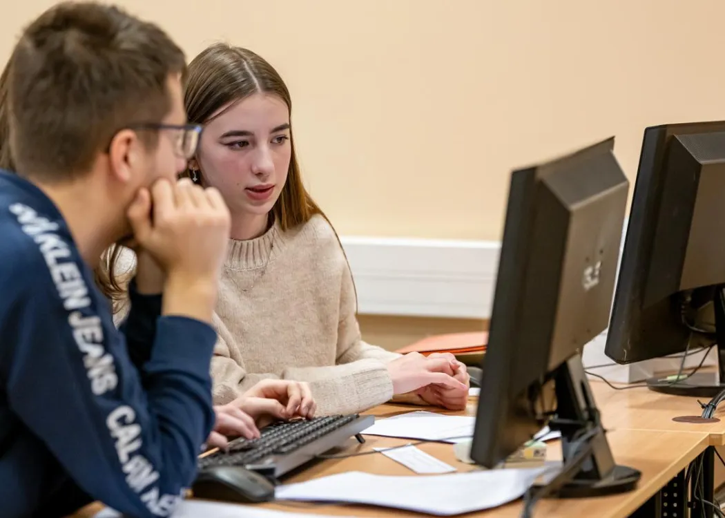 Młodzież siedzi przy komputerze podczas zespołowych zawodów programowania