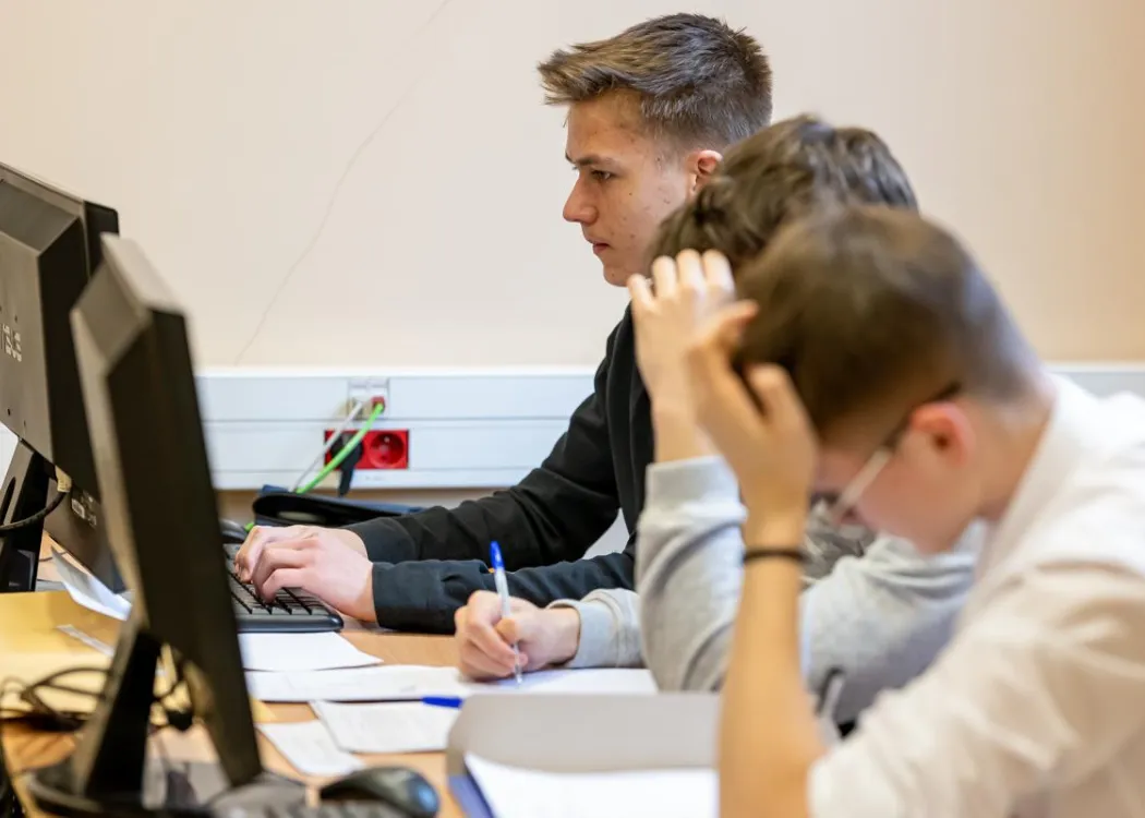 Młodzież siedzi przy komputerze podczas zespołowych zawodów programowania