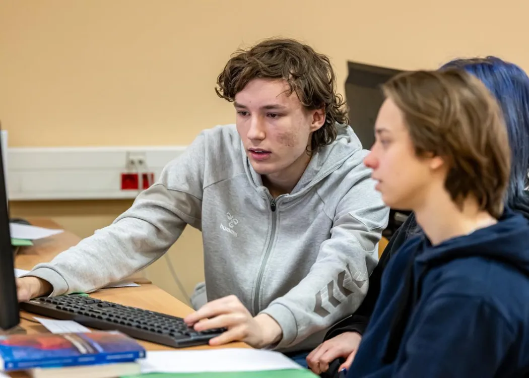 Młodzież siedzi przy komputerze podczas zespołowych zawodów programowania