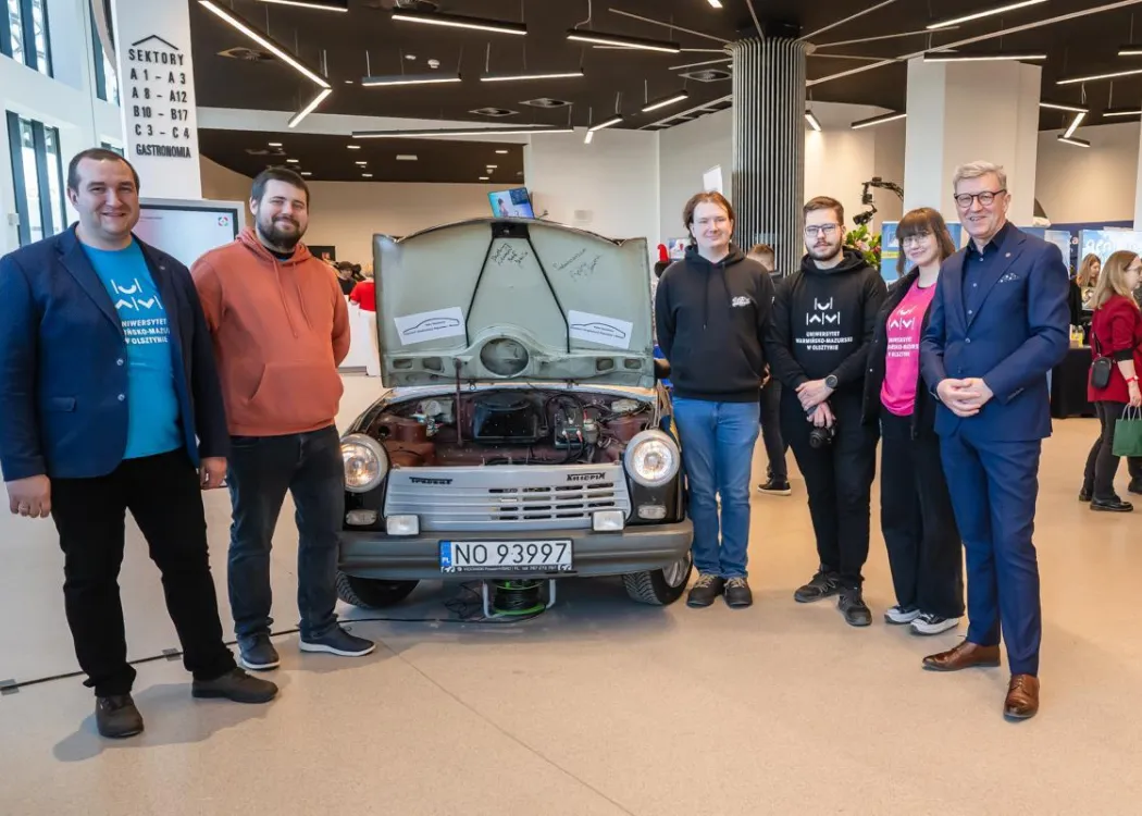 Warmia Inspiration 2026: studenci pozują do zdjęcia przy elektrycznym Trabancie z prof. Jerzym Przyborowskim, rektorem UWM