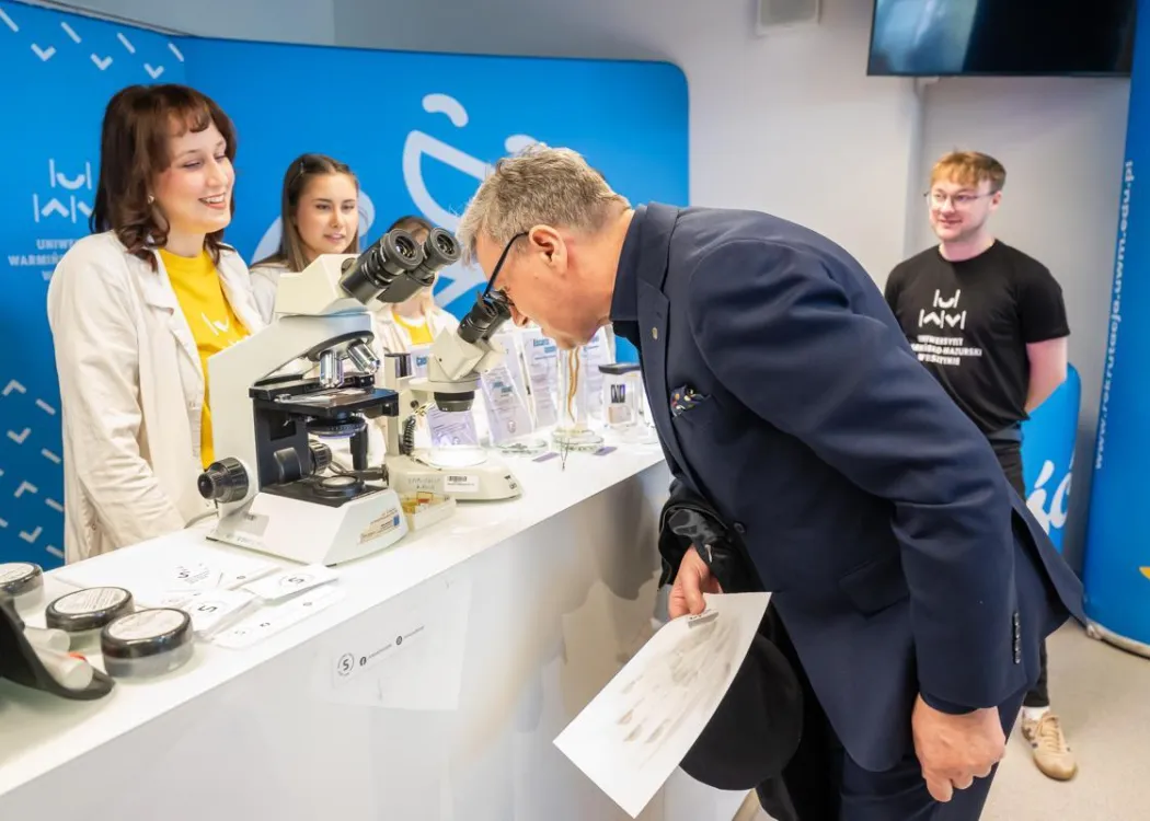 prof. Jerzy Przyborowski patrzy w mikroskop na jednym ze stoisk UWM