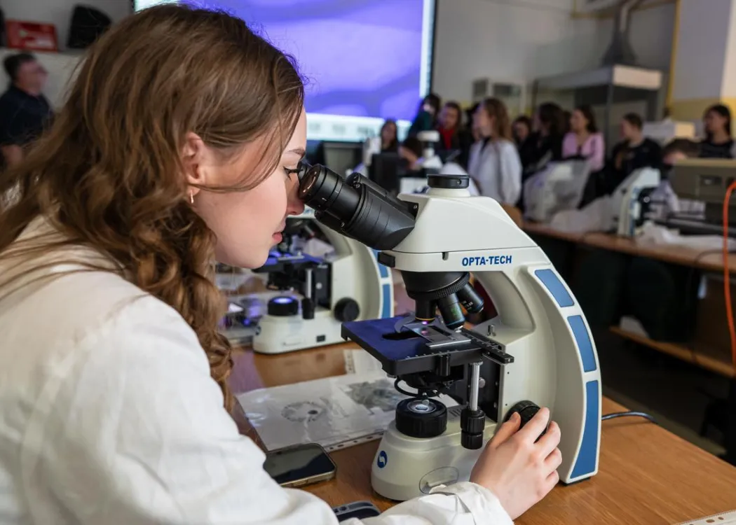 Dzień Otwarty UWM 2026: uczestniczka wydarzenia patrzy w mikroskop